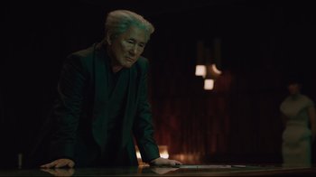 Movie still from “Ghost in the Shell” (2017), directed by Rupert Sanders – An older man leaning on a table in a dark room; Medium shot, Low angle