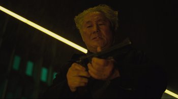 Movie still from “Ghost in the Shell” (2017), directed by Rupert Sanders – An older man holding a gun in a dark room; Close Up shot, Low angle