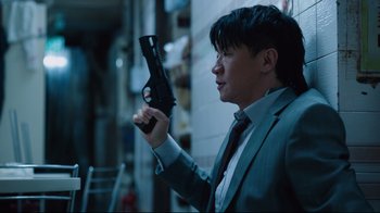 Movie still from “Ghost in the Shell” (2017), directed by Rupert Sanders – A man in a suit and tie holding a gun in his hand; Medium shot, Low angle