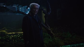 Movie still from “Ghost in the Shell” (2017), directed by Rupert Sanders – An older man standing in the dark near a tree; Medium shot, Over the shoulder angle