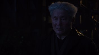 Movie still from “Ghost in the Shell” (2017), directed by Rupert Sanders – An older man with a blue hair and a black robe; Close Up shot, Over the shoulder angle