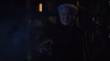 Movie still from “Ghost in the Shell” (2017), directed by Rupert Sanders – An older man holding a gun in a dark room; Close Up shot, Over the shoulder angle