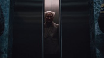 Movie still from “Ghost in the Shell” (2017), directed by Rupert Sanders – An older man wearing a suit in an elevator; Medium shot, Low angle