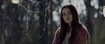A young woman standing next to a tree in the woods