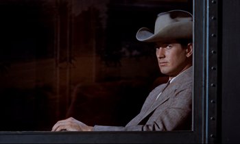 Movie still from “Giant” (1956), directed by George Stevens – A man wearing a cowboy hat sitting in front of a couch; Medium shot, Low angle