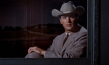 Movie still from “Giant” (1956), directed by George Stevens – A man wearing a cowboy hat sitting in a chair; Medium shot, Low angle