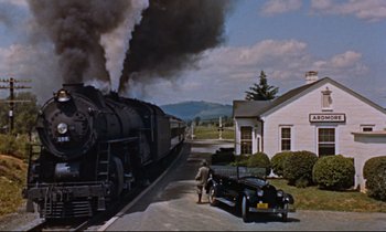 Movie still from “Giant” (1956), directed by George Stevens – A man walking next to a car near a train; Extreme Wide shot, Low angle