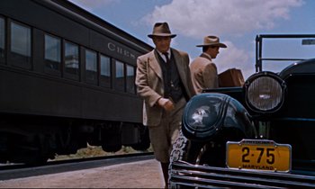 Movie still from “Giant” (1956), directed by George Stevens – A man in a suit and hat standing next to a car; Wide shot, Low angle