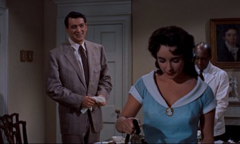 Movie still from “Giant” (1956), directed by George Stevens – A man in a suit and tie standing next to a woman in a blue dress; Medium shot, Over the shoulder angle