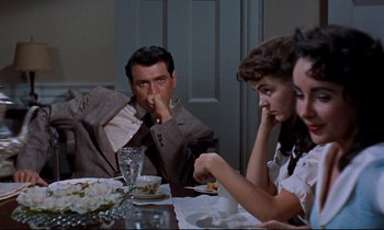 Movie still from “Giant” (1956), directed by George Stevens – A group of people sitting at a dinner table; Medium shot, Over the shoulder angle