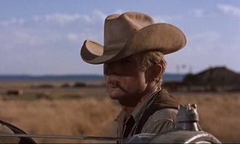 Movie still from “Giant” (1956), directed by George Stevens – A man in a cowboy hat is standing next to a fence; Close Up shot, Low angle