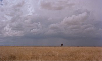 Movie still from “Giant” (1956), directed by George Stevens – A person riding a horse through a field under a cloudy sky; Extreme Wide shot, Low angle