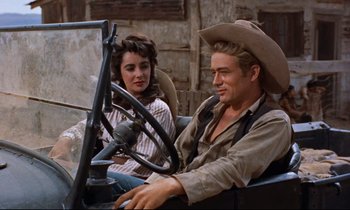 Movie still from “Giant” (1956), directed by George Stevens – A man and a woman sitting in the driver's seat of an old car; Medium shot, Over the shoulder angle