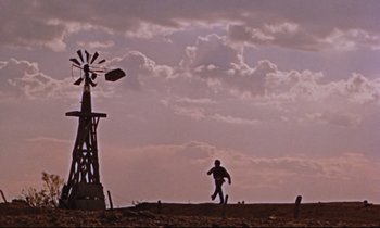 Movie still from “Giant” (1956), directed by George Stevens – A man running on a dirt road near a windmill; Extreme Wide shot, Low angle