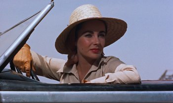 Movie still from “Giant” (1956), directed by George Stevens – A woman with a straw hat sitting in the back of a car; Close Up shot, Low angle