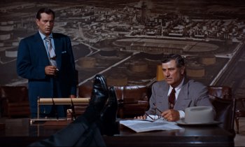 Movie still from “Giant” (1956), directed by George Stevens – Two men sitting at a table in front of a painting; Wide shot, Over the shoulder angle