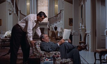 Movie still from “Giant” (1956), directed by George Stevens – A man sitting in a chair next to another man; Medium shot, High angle