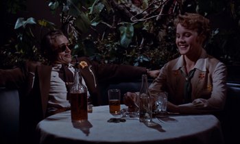 Movie still from “Giant” (1956), directed by George Stevens – Two people are sitting at a table with drinks; Medium shot, High angle
