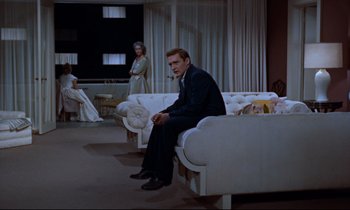 Movie still from “Giant” (1956), directed by George Stevens – A man sitting on top of a couch in a living room; Wide shot, High angle