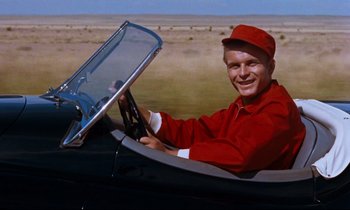 Movie still from “Giant” (1956), directed by George Stevens – A man driving a car in a field; Medium shot, Low angle