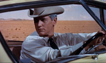 Movie still from “Giant” (1956), directed by George Stevens – A man wearing a cowboy hat sitting in the driver's seat of a car; Medium shot, Low angle