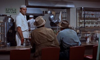 Movie still from “Giant” (1956), directed by George Stevens – A group of men sitting at a table in a kitchen; Medium shot, Over the shoulder angle