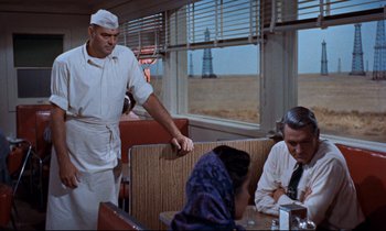 Movie still from “Giant” (1956), directed by George Stevens – A man standing in front of two people in a restaurant; Medium shot, Over the shoulder angle