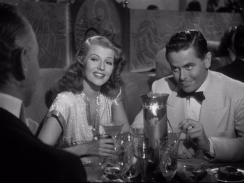 Movie still from “Gilda” (1946), directed by Charles Vidor – A man and a woman sitting at a table with drinks; Medium shot, Low angle