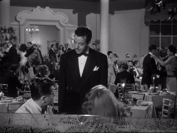 Movie still from “Gilda” (1946), directed by Charles Vidor – A black and white photo of a man in a tuxedo at a restaurant; Medium shot, Over the shoulder angle