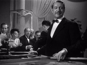 Movie still from “Gilda” (1946), directed by Charles Vidor – A man standing at a table in front of people; Medium shot, Low angle