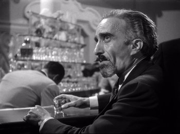 Movie still from “Gilda” (1946), directed by Charles Vidor – An older man sitting at a table with a glass of wine; Close Up shot, Low angle