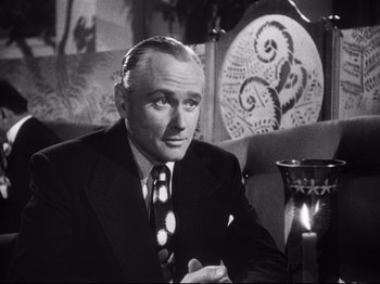 Movie still from “Gilda” (1946), directed by Charles Vidor – An older man in a suit and tie sitting at a table; Close Up shot, Low angle