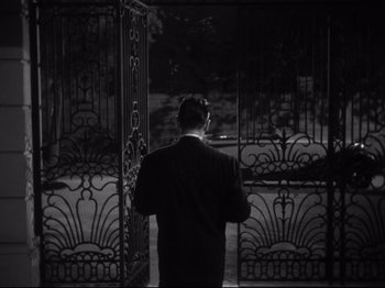 Movie still from “Gilda” (1946), directed by Charles Vidor – A black and white photo of a man standing in front of a gate; Medium shot, High angle