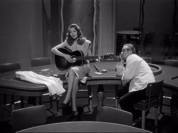 Movie still from “Gilda” (1946), directed by Charles Vidor – A man and a woman sitting at a table with a guitar; Medium shot, High angle