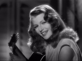 Movie still from “Gilda” (1946), directed by Charles Vidor – A beautiful woman holding a guitar and smiling for the camera; Close Up shot, Over the shoulder angle
