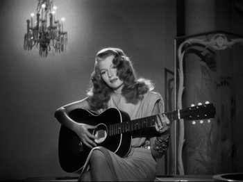 Movie still from “Gilda” (1946), directed by Charles Vidor – A woman sitting down with a guitar in her hands; Medium shot, Low angle