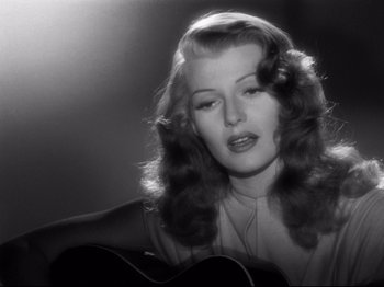 Movie still from “Gilda” (1946), directed by Charles Vidor – A black - and - white photo of a woman holding a guitar; Close Up shot, Over the shoulder angle