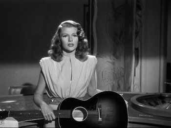 Movie still from “Gilda” (1946), directed by Charles Vidor – A black and white photo of a woman holding a guitar; Medium shot, Low angle