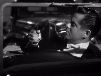 Movie still from “Gilda” (1946), directed by Charles Vidor – A black and white photo of a man smoking a cigarette; Close Up shot, High angle