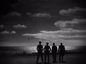 Movie still from “Gilda” (1946), directed by Charles Vidor – A group of men standing next to each other on the beach; Extreme Wide shot, Low angle