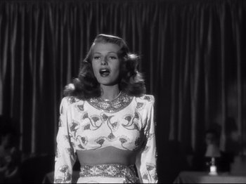 Movie still from “Gilda” (1946), directed by Charles Vidor – A woman is singing into a microphone in a black and white photo; Medium shot, Low angle