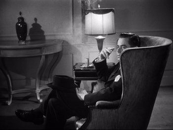 Movie still from “Gilda” (1946), directed by Charles Vidor – A black and white photo of a man smoking a cigarette; Medium shot, High angle