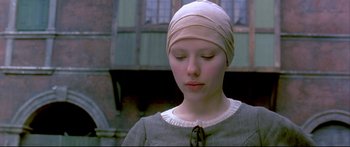 Movie still from “Girl with a Pearl Earring” (2003), directed by Peter Webber – A young girl wearing a head covering is looking down at the ground; Close Up shot, Low angle