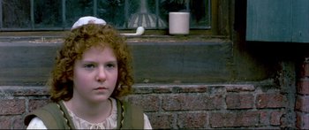 Movie still from “Girl with a Pearl Earring” (2003), directed by Peter Webber – A young girl with a red curly hair standing in front of a brick wall; Close Up shot, High angle