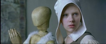 Movie still from “Girl with a Pearl Earring” (2003), directed by Peter Webber – A young girl wearing a white bonnet and a wooden dummy; Close Up shot, Low angle