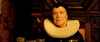 Movie still from “Girl with a Pearl Earring” (2003), directed by Peter Webber – An older woman wearing a white collar and a black dress; Close Up shot, Low angle
