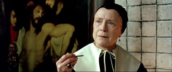 Movie still from “Girl with a Pearl Earring” (2003), directed by Peter Webber – An older woman in a black and white outfit holding a paintbrush in front of a painting; Close Up shot, Low angle