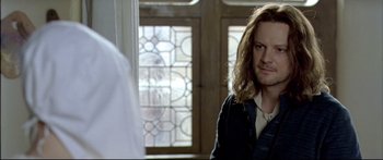 Movie still from “Girl with a Pearl Earring” (2003), directed by Peter Webber – A man standing in front of a stained glass window in a room; Close Up shot, Over the shoulder angle