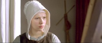 Movie still from “Girl with a Pearl Earring” (2003), directed by Peter Webber – A young woman wearing a white hood and a brown vest; Close Up shot, Low angle