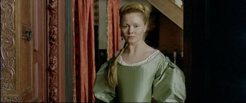 Movie still from “Girl with a Pearl Earring” (2003), directed by Peter Webber – A woman in a green dress standing in front of a red curtain; Medium shot, Over the shoulder angle